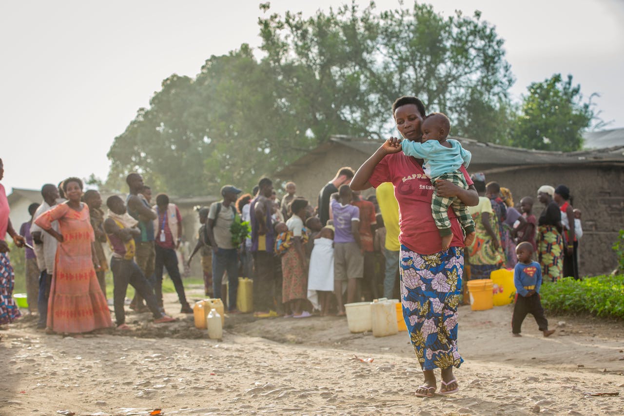People gather with containers for water in a rural Burundian village, depicting daily life.