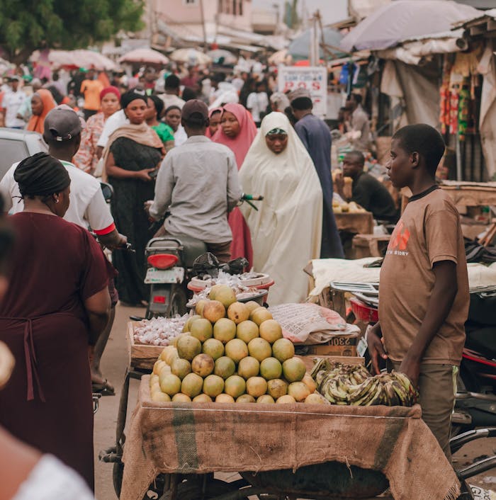 Lively African market scene featuring a fruit vendor and diverse crowd in vibrant attire.